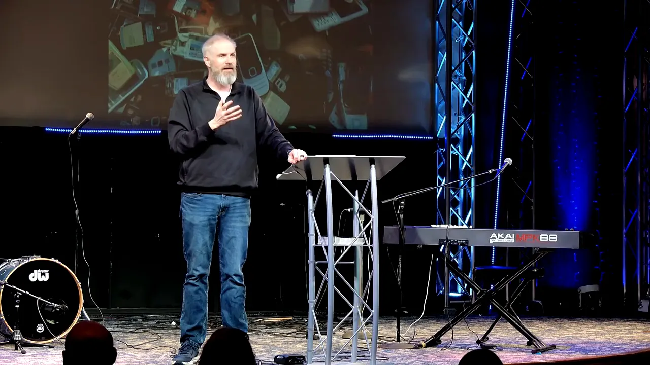 Speaker on stage at a lectern gesturing while delivering a sermon about scripture and culture.