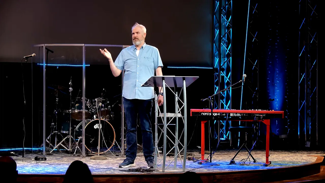 Speaker addressing the audience on stage with modern lighting and musical instruments