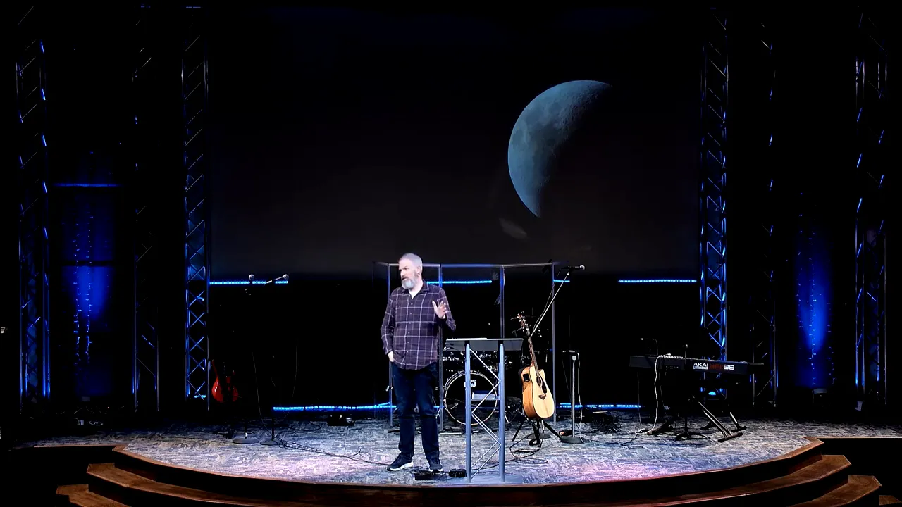 Church speaker on stage with a large half-moon projected on the screen behind him