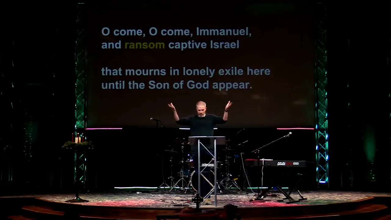 Stage with projected hymn lyrics 'O come, O come, Immanuel' above a worship leader at the lectern