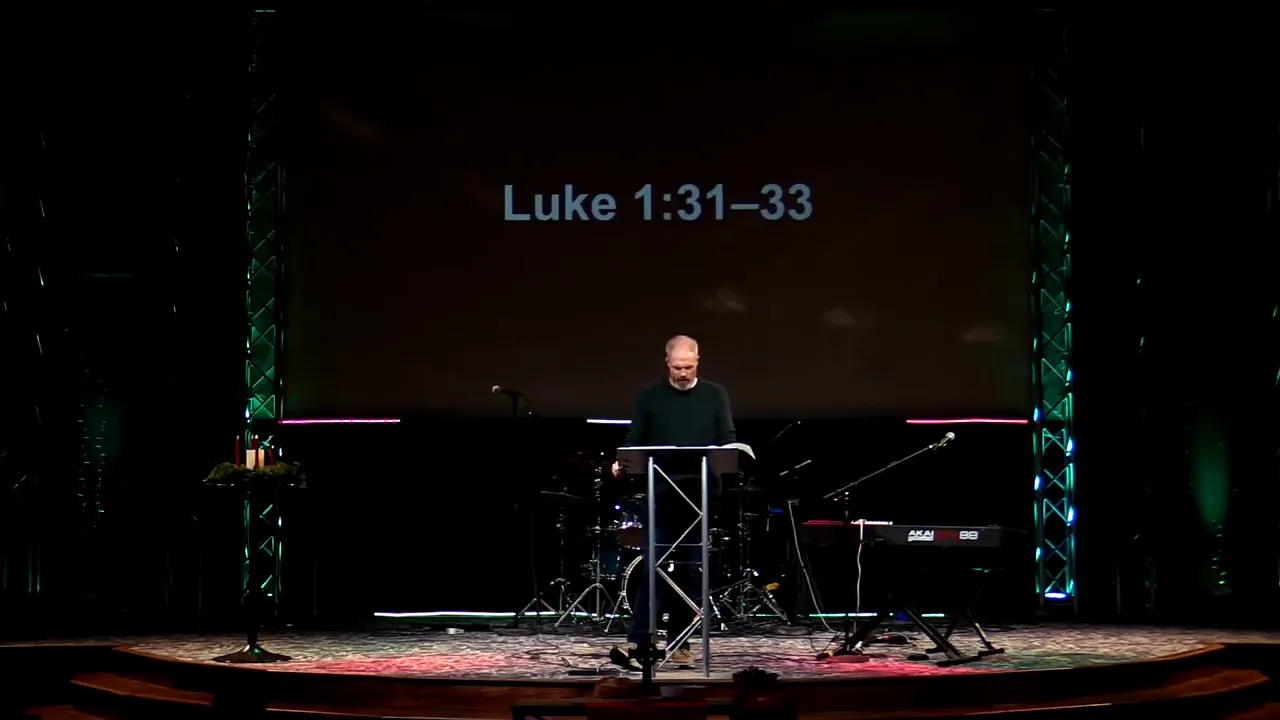Stage with 'Luke 1:31–33' projected above a preacher at a lectern with Advent candles visible to the left