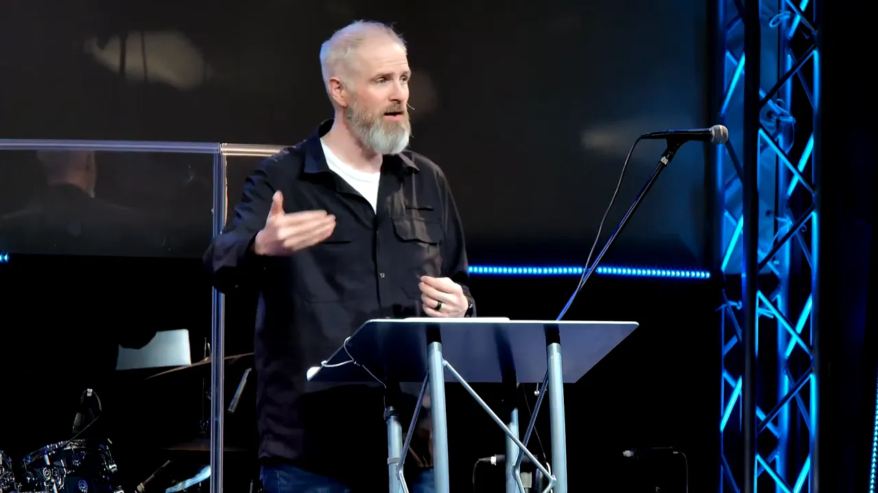 speaker at lectern gesturing invitingly during a sermon about Jesus as the living bridge