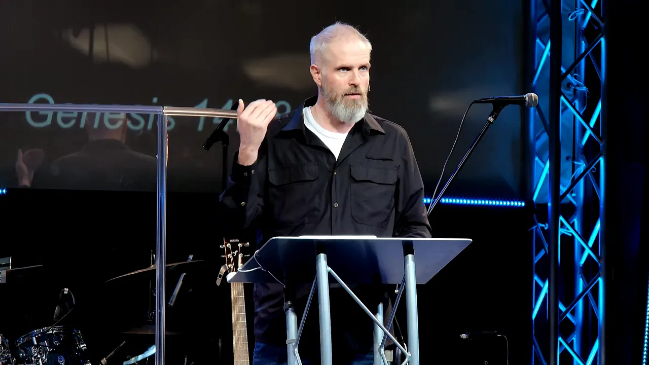 Preacher at lectern with hand raised, clear lighting and sharp focus, blue stage truss at right