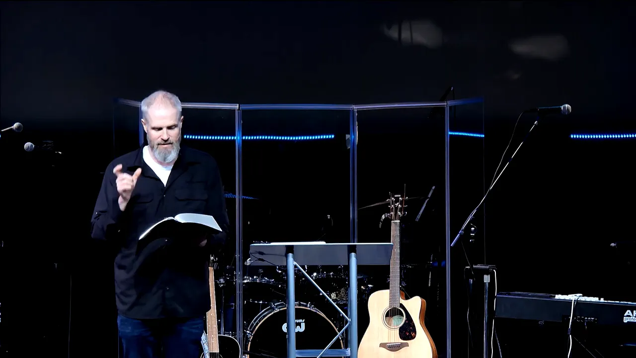 Speaker reading from an open Bible at a church lectern, mid-sermon, with instruments on stage