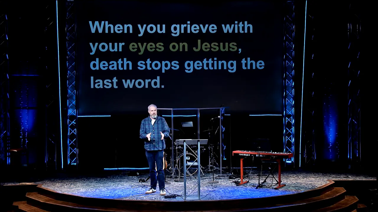 Pastor speaking on stage with a screen displaying “When you grieve with your eyes on Jesus, death stops getting the last word.”