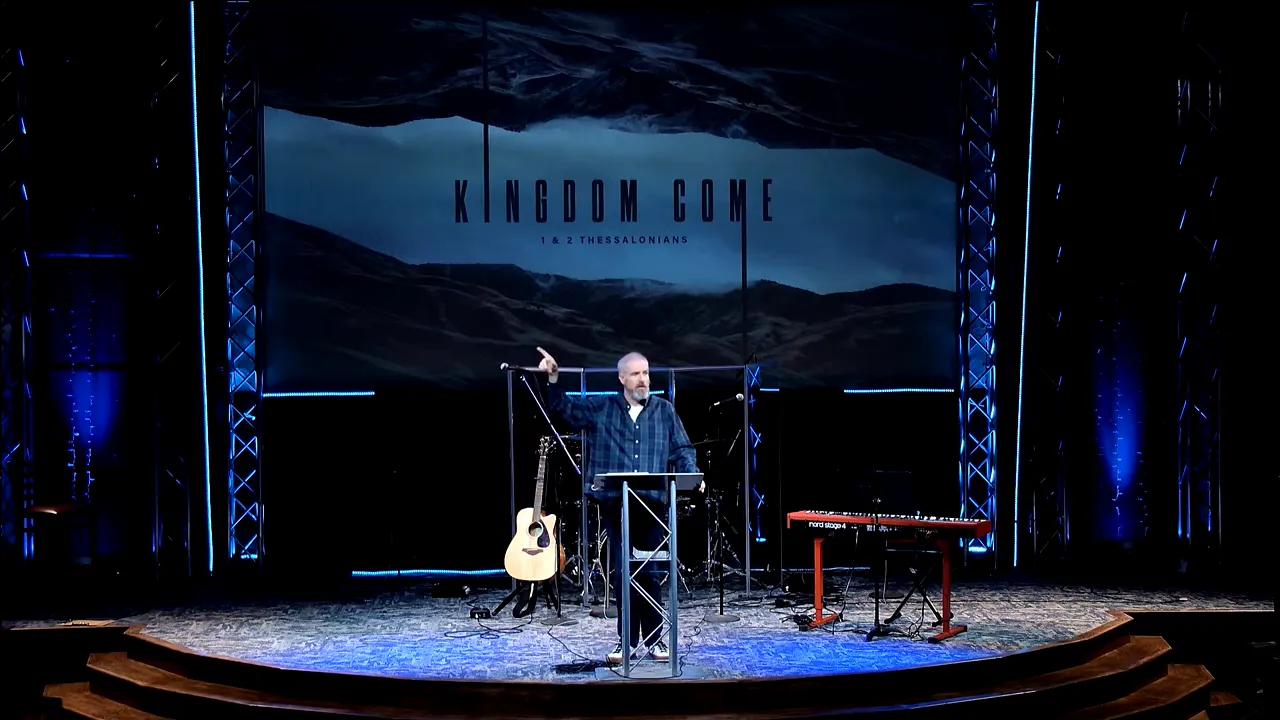 Church speaker standing at a lectern with hands outstretched under “Kingdom Come”