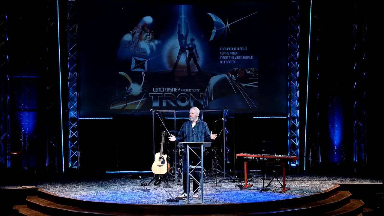 Speaker standing at a podium on a Tron themed stage with keyboard and guitars