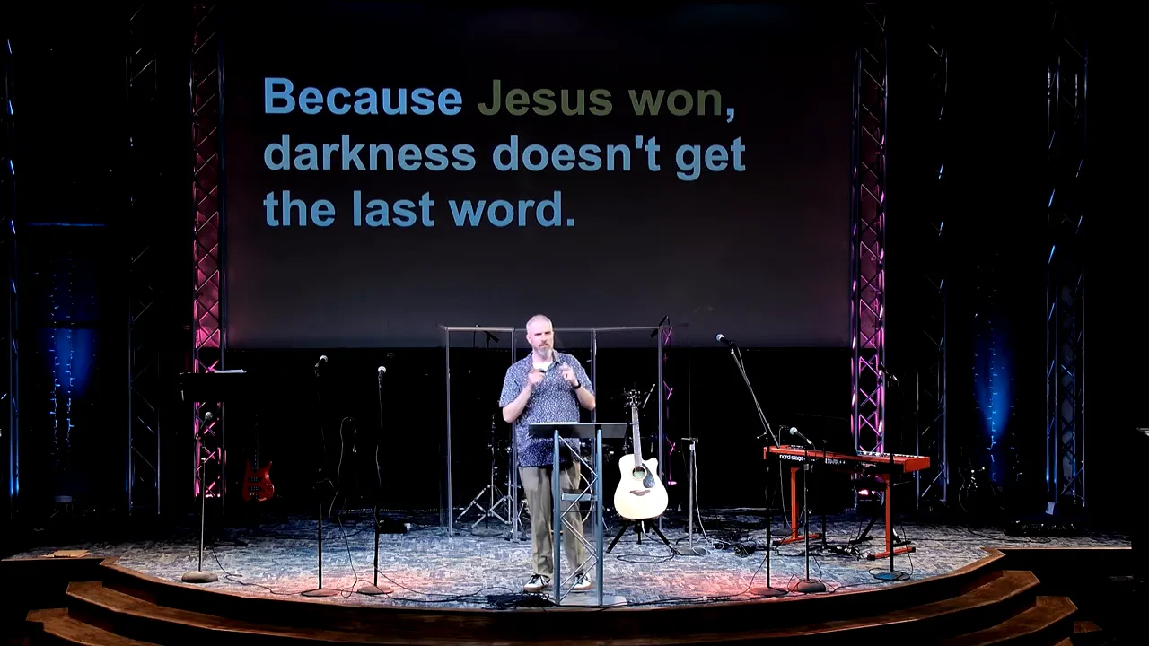 Church stage speaker gesturing with backdrop text “Because Jesus won, darkness doesn't get the last word.”