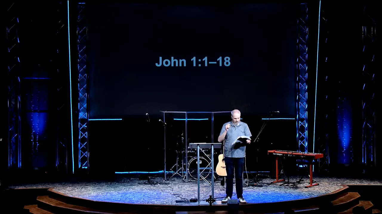 Church speaker teaching from a Bible with “John 1:1–18” on the presentation screen