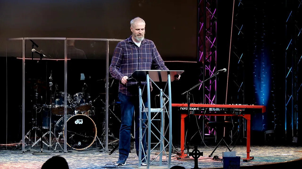 Speaker standing at a lectern with stage lights and drum set behind him