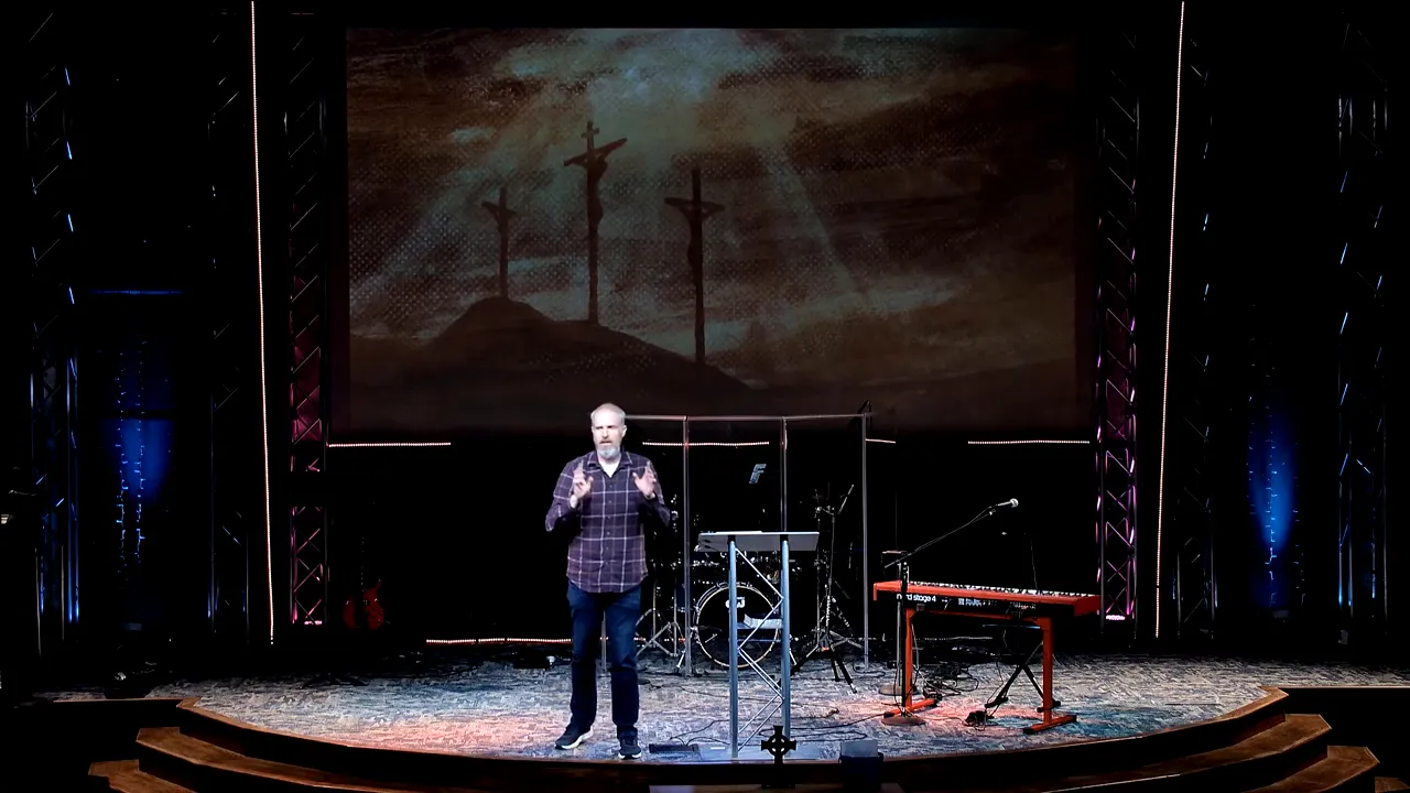 Speaker on a church stage in front of a large backdrop of crosses, discussing Jesus’ cry from the cross.