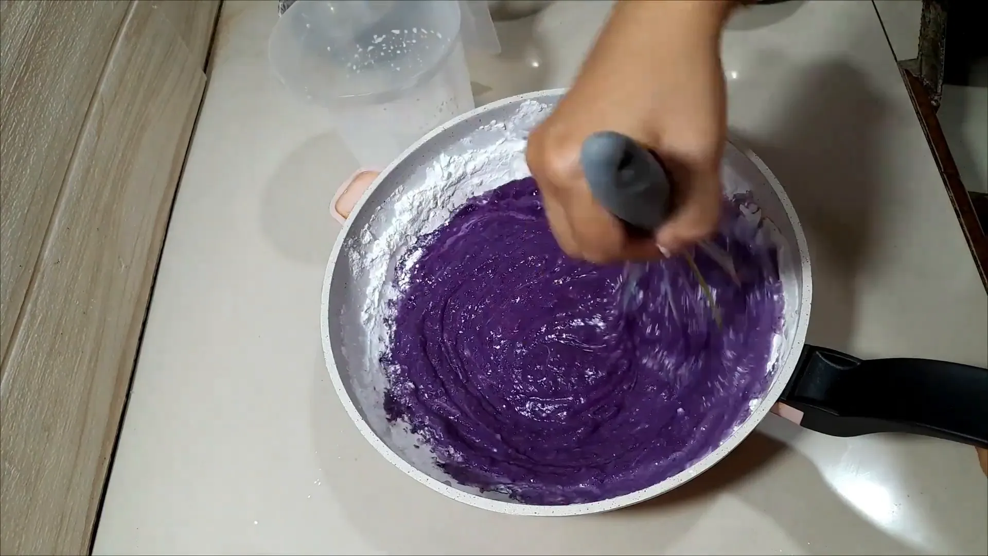 Memasak adonan kue ubi ungu di atas wajan sambil diaduk