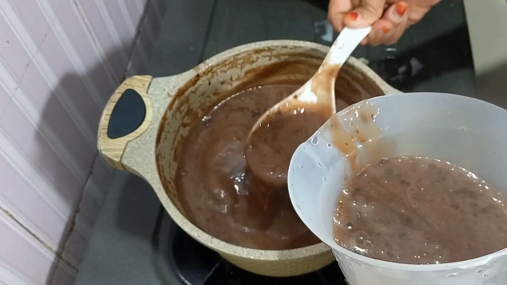 Menuang puding coklat ke dalam cetakan menggunakan gelas takar