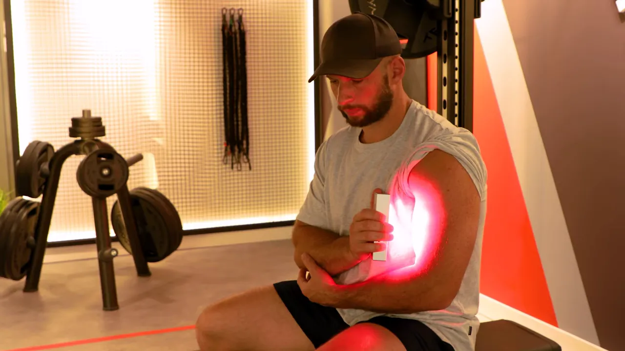 Person using a compact handheld red light device on their elbow for spot treatment