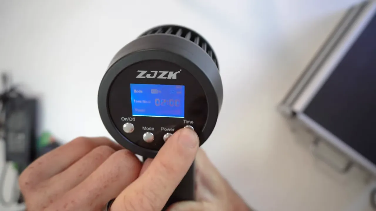 Close-up of a handheld red light device control panel with a finger pressing the time button