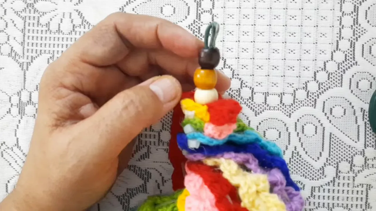 A hand holding the gathered crochet end beneath pale, golden-brown, and dark beads with a metal loop above them