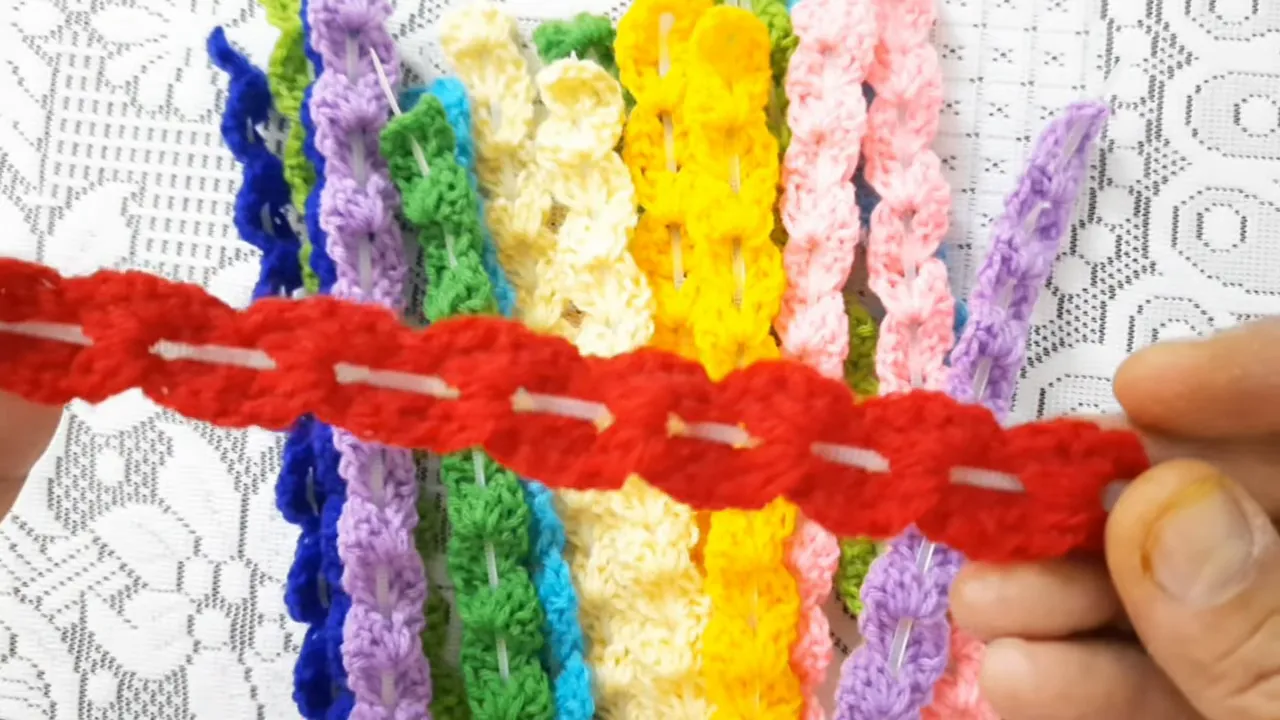 Hands holding a red scalloped crochet strip with a pale cable tie visible through its center openings