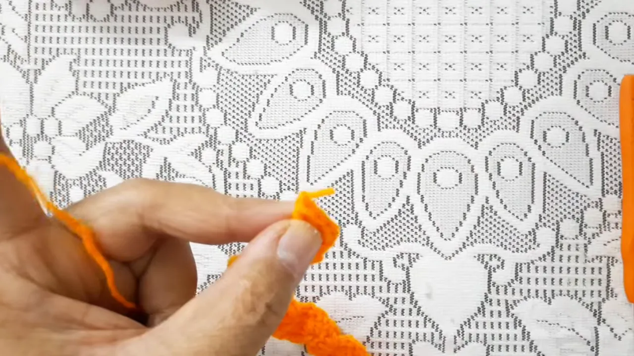 An orange-yellow scalloped crochet strip lying horizontally on a lace-covered surface