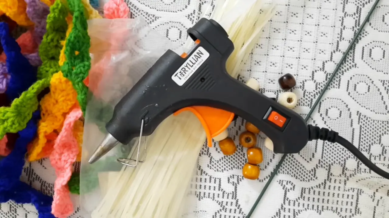 Crochet strips, pale cable ties, loose beads, a slender metal support, and a hot glue gun on a lace-covered surface