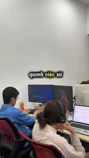 Hai lập trình viên làm việc trước màn hình hiển thị mã nguồn trong văn phòng