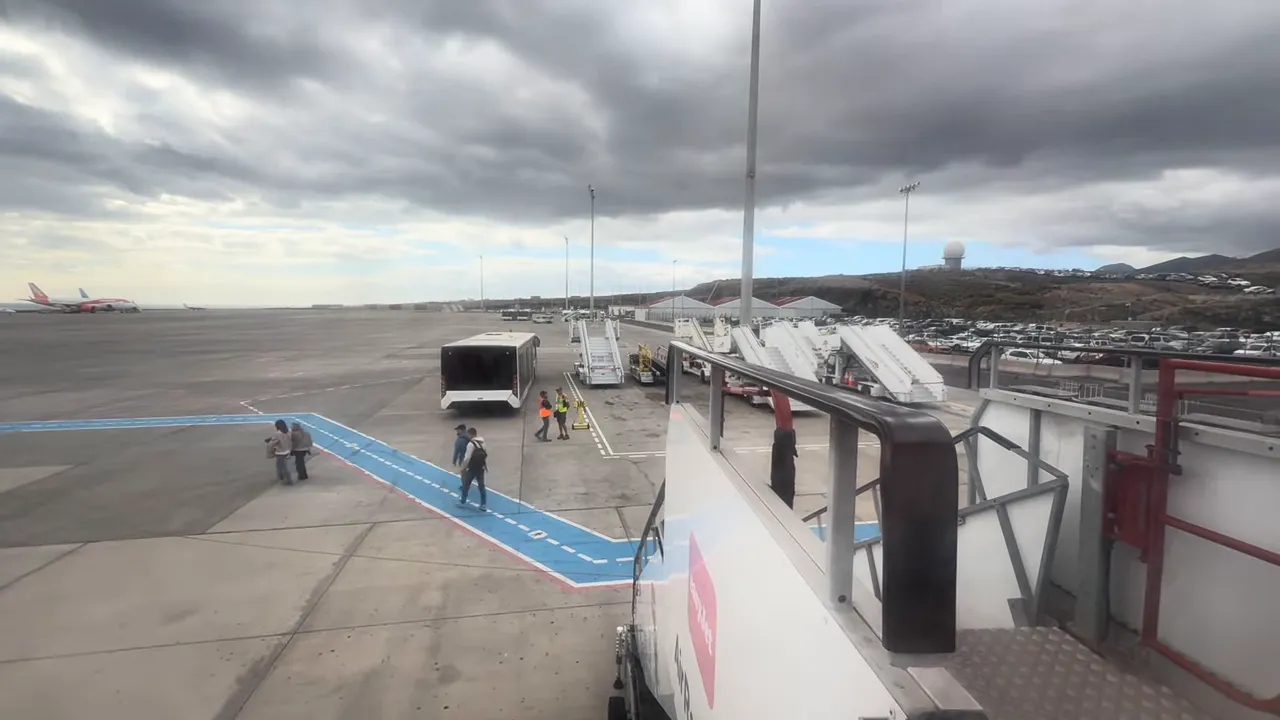 I Almost Missed My Flight - Tenerife South Airport Delays and How to Avoid the Stress 6 Wide view of Tenerife South apron showing mobile stairs, an airport transfer bus and cloudy sky