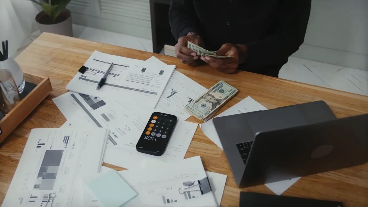 Overhead view of a desk with printed financial charts, a phone calculator app, cash and a laptop — preparing loan decisions.