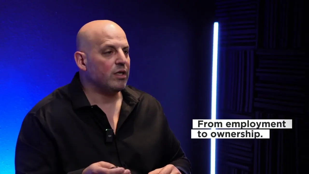 Speaker in blue-lit studio with on-screen text 'From employment to ownership.'