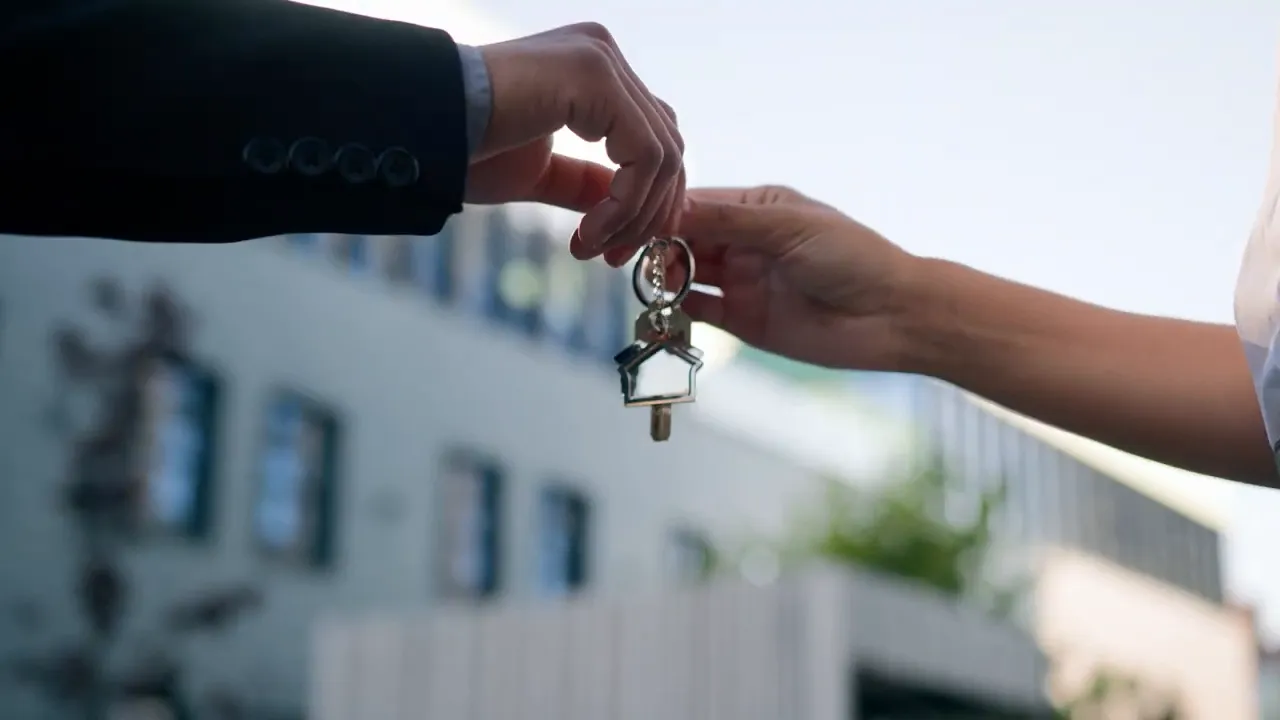 Two hands exchanging a keychain with a house-shaped charm representing a business or property sale