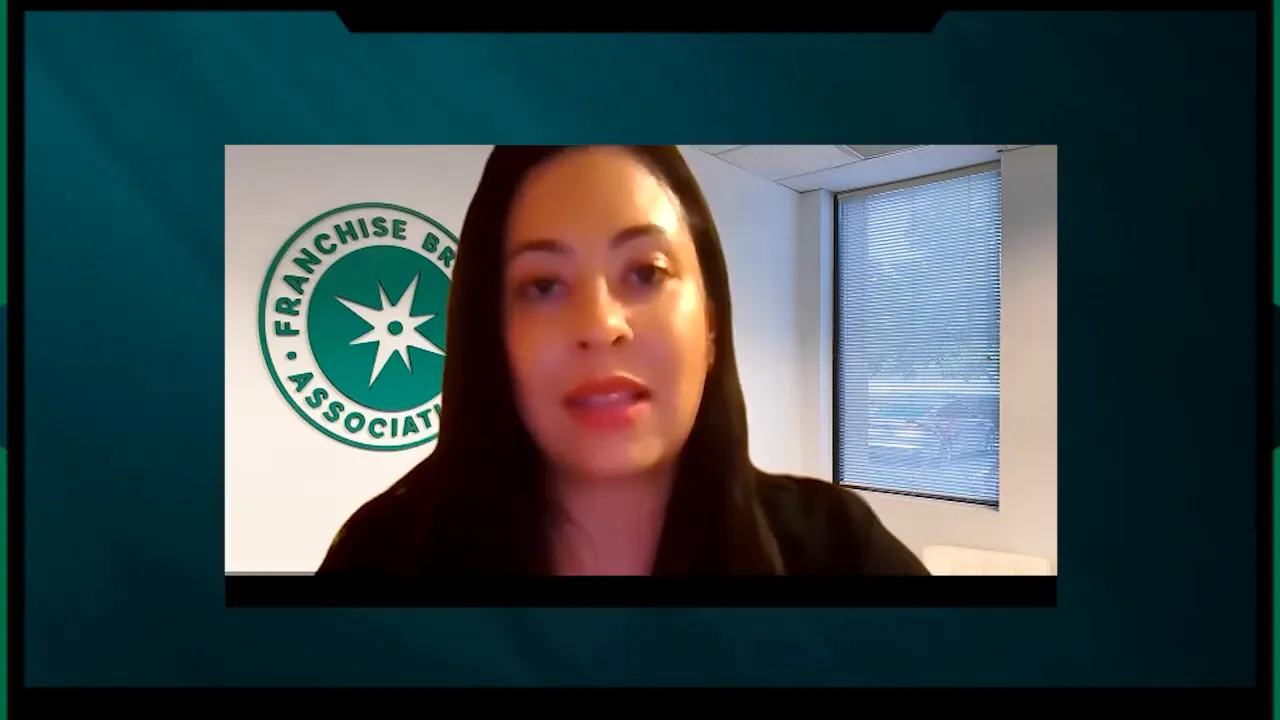 Clear video frame of a presenter discussing franchise vs independent business models with logo and office window behind
