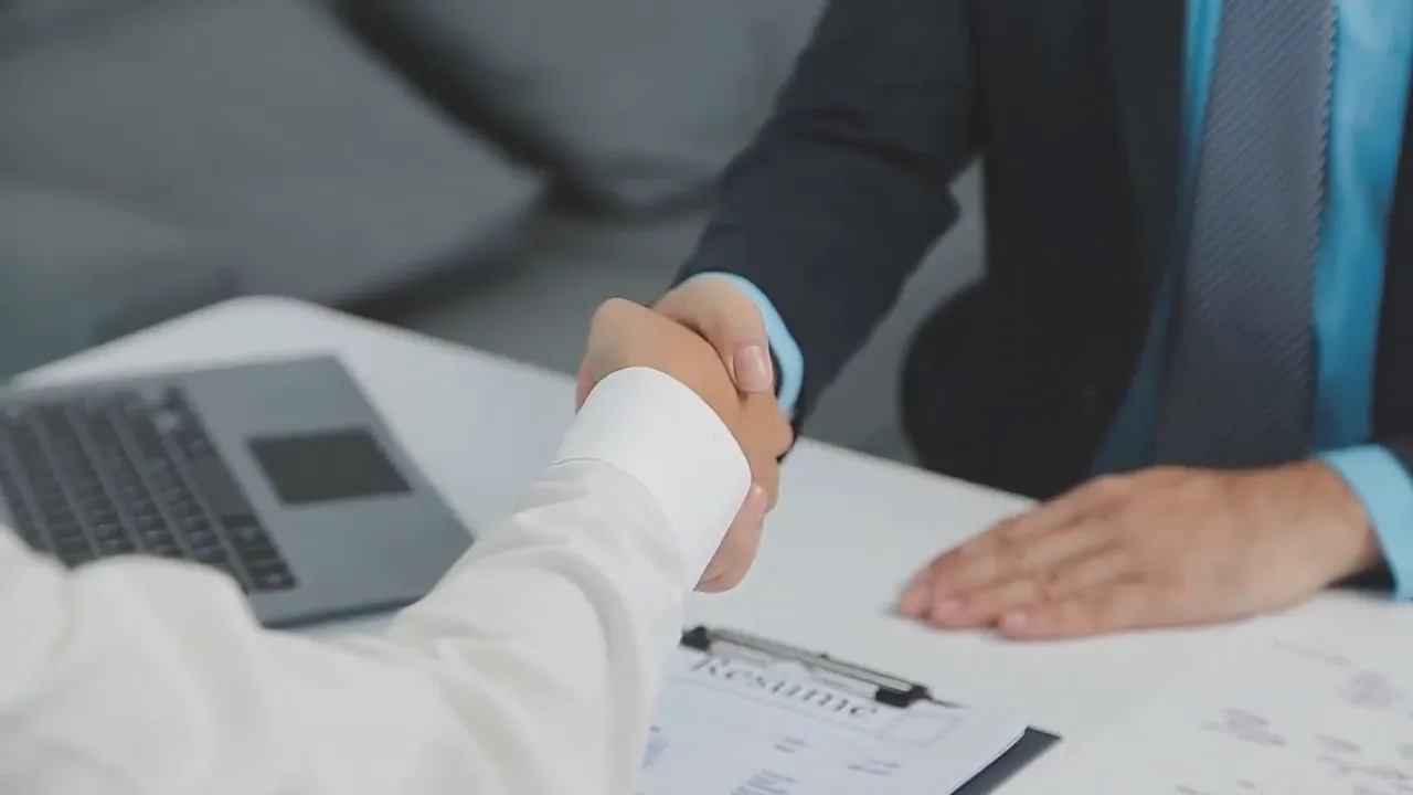 Handshake over a contract and laptop representing a franchise agreement and CEO-model partnership