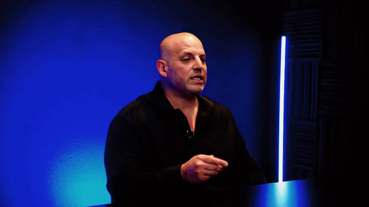 Podcast host speaking in a studio with blue backlight, explaining advantages of buying a business