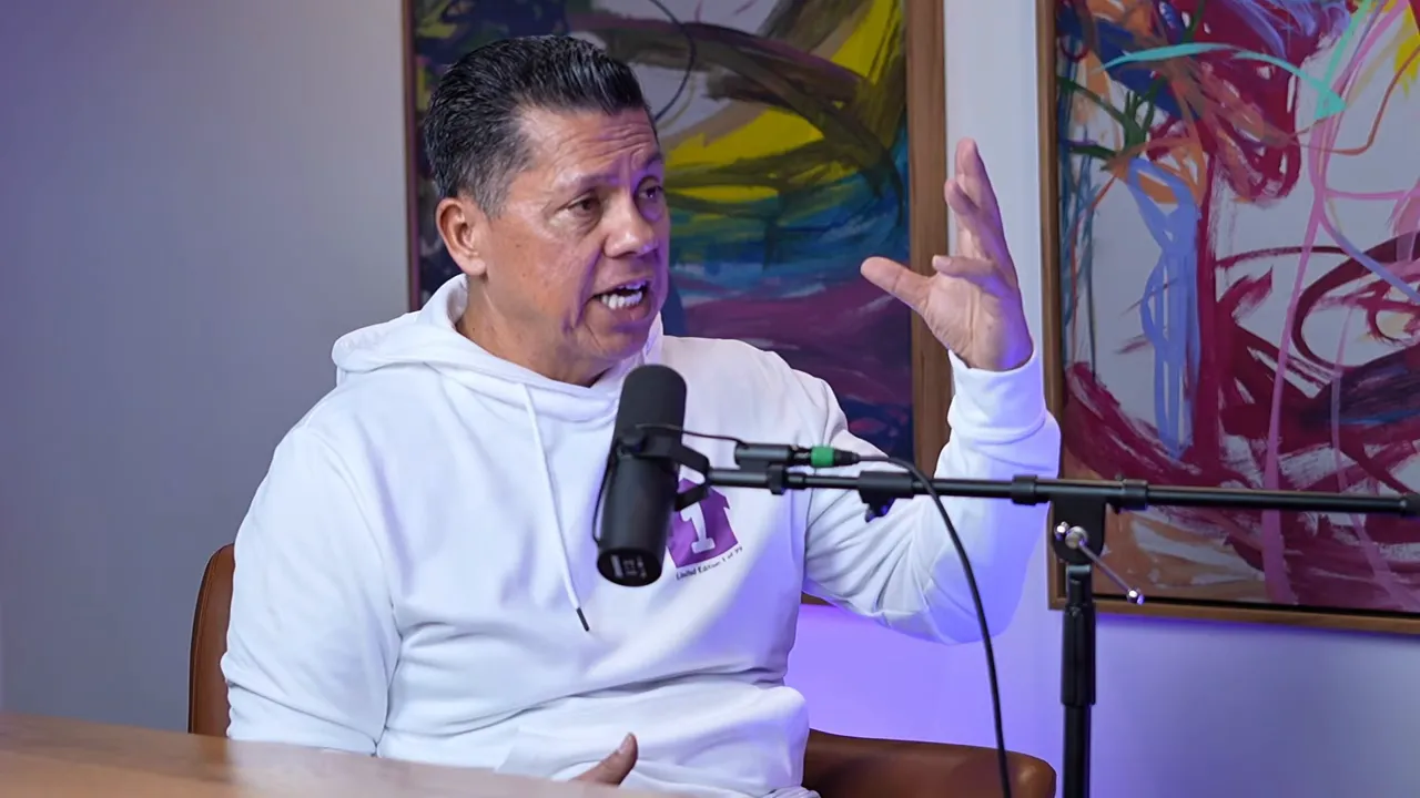 Podcast speaker animatedly gesturing with hand raised while talking into a microphone, colorful paintings in background