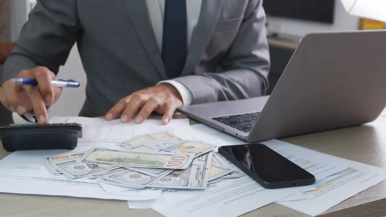 Desk with cash bills, calculator, laptop and smartphone representing business finances and cash flow