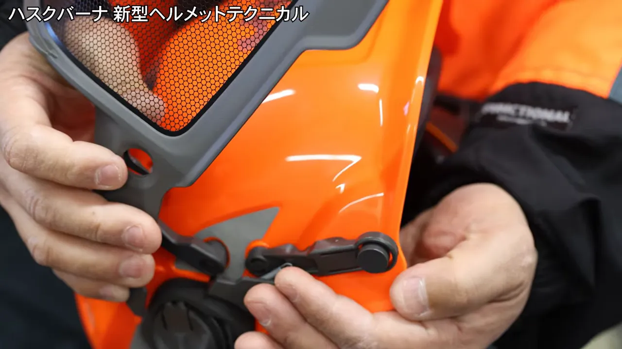 オレンジ色のヘルメット側面で丸い固定部を指で押している様子
