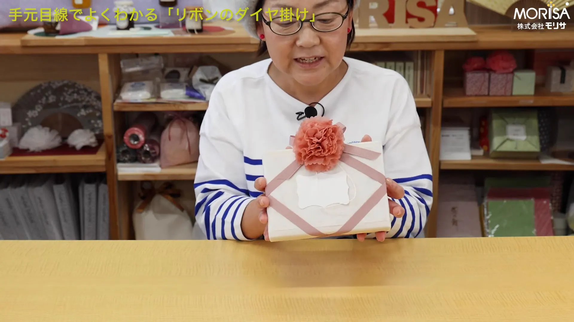 ダイヤ掛けを施した箱を両手で持ち、中央に造花のオーナメントが付いた完成見本のクローズアップ。