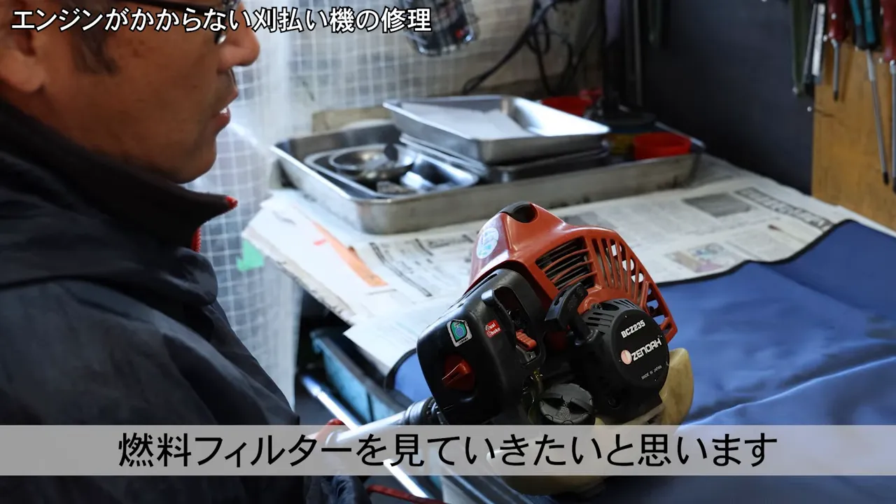 刈払機本体を手に、これから燃料フィルターを確認すると説明する場面