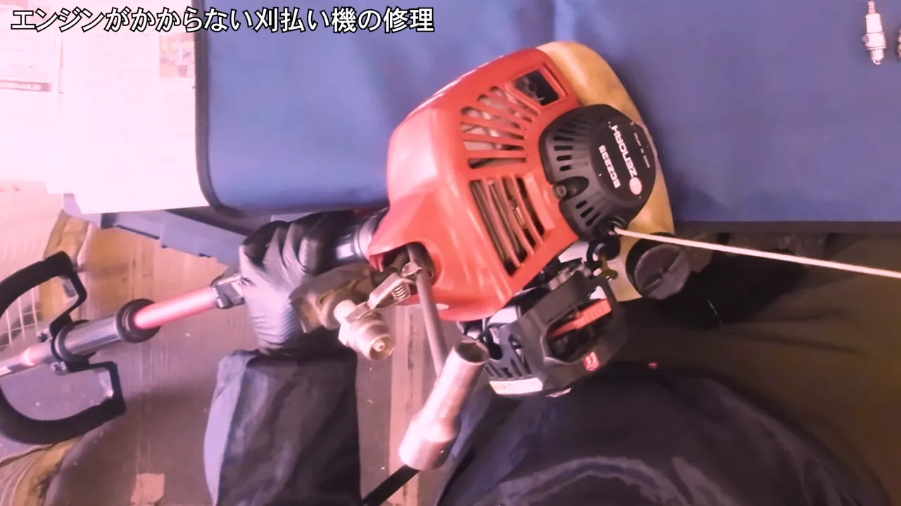 刈払い機のプラグ付近に点火テスターのプローブを当てて火花を確認している作業風景