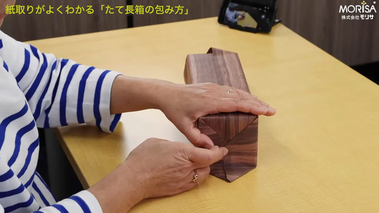 包装紙の角を三角形に折り、指で重なりを整えているクローズアップ写真。