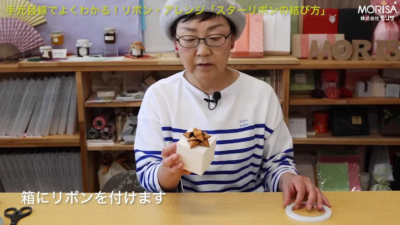 スターリボンを載せた箱を持ち片手で両面テープを取ろうとしている手元