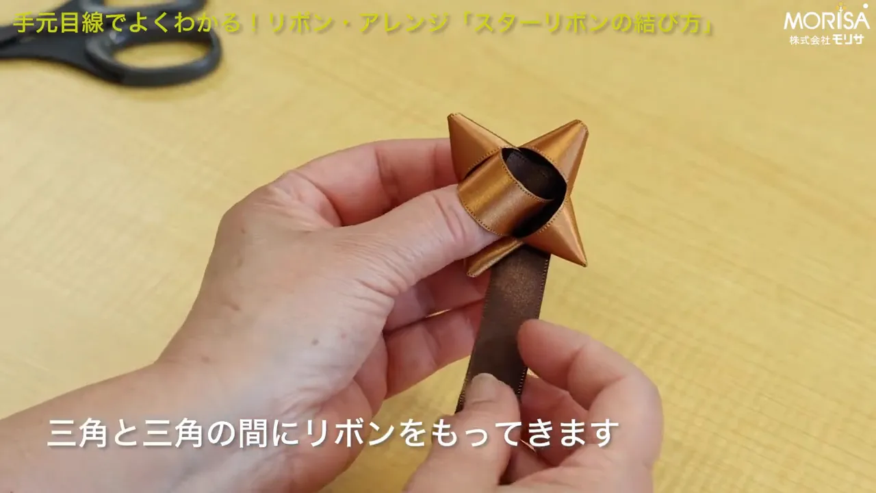 リボンを三角の間に通して重ねる手元の作業の写真