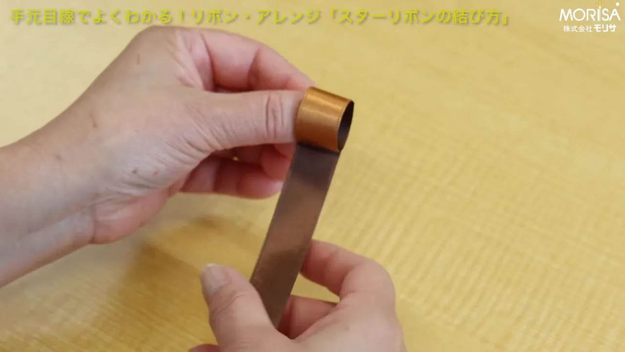 親指に一周巻かれたリボンのループと下に垂れたリボンがはっきり見える手元の写真