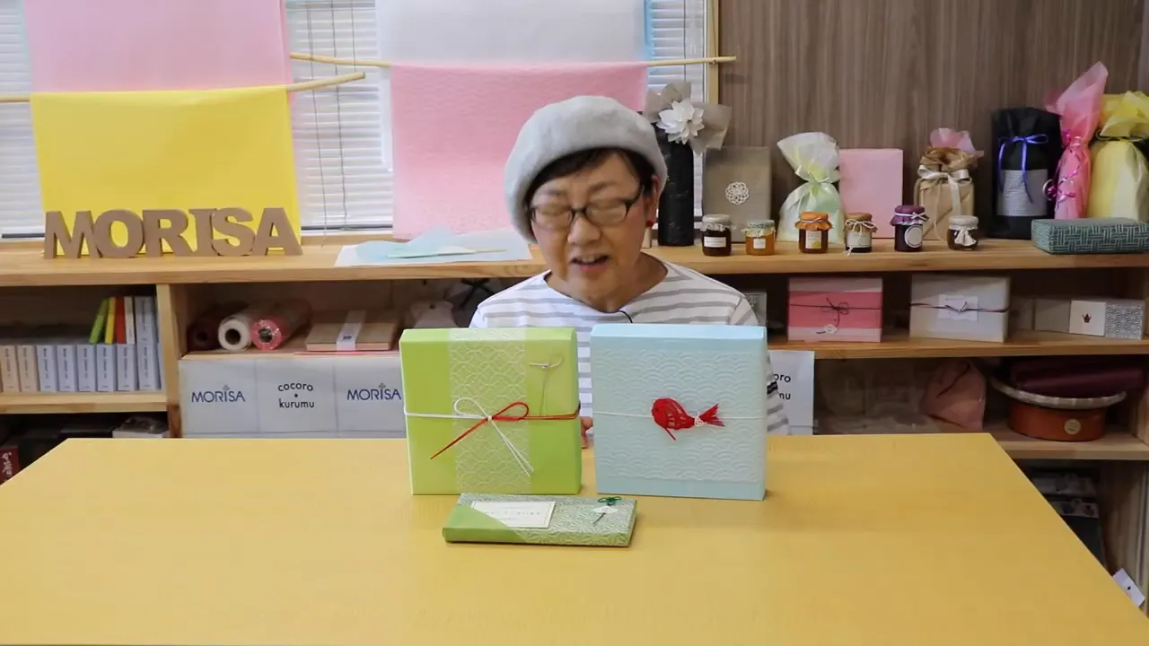 包装済みのギフトボックスが机に並び、作り手が後ろにいる風景の写真