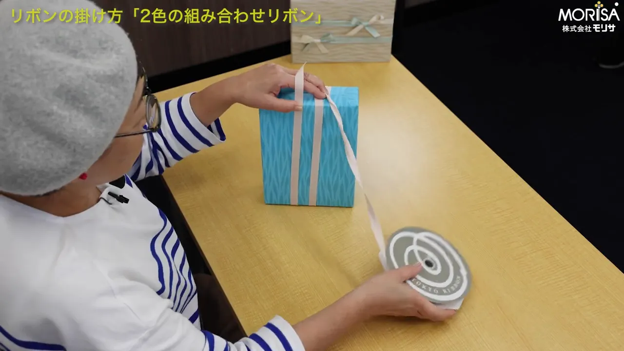 箱にリボンを巻き付けて長さを測るカット