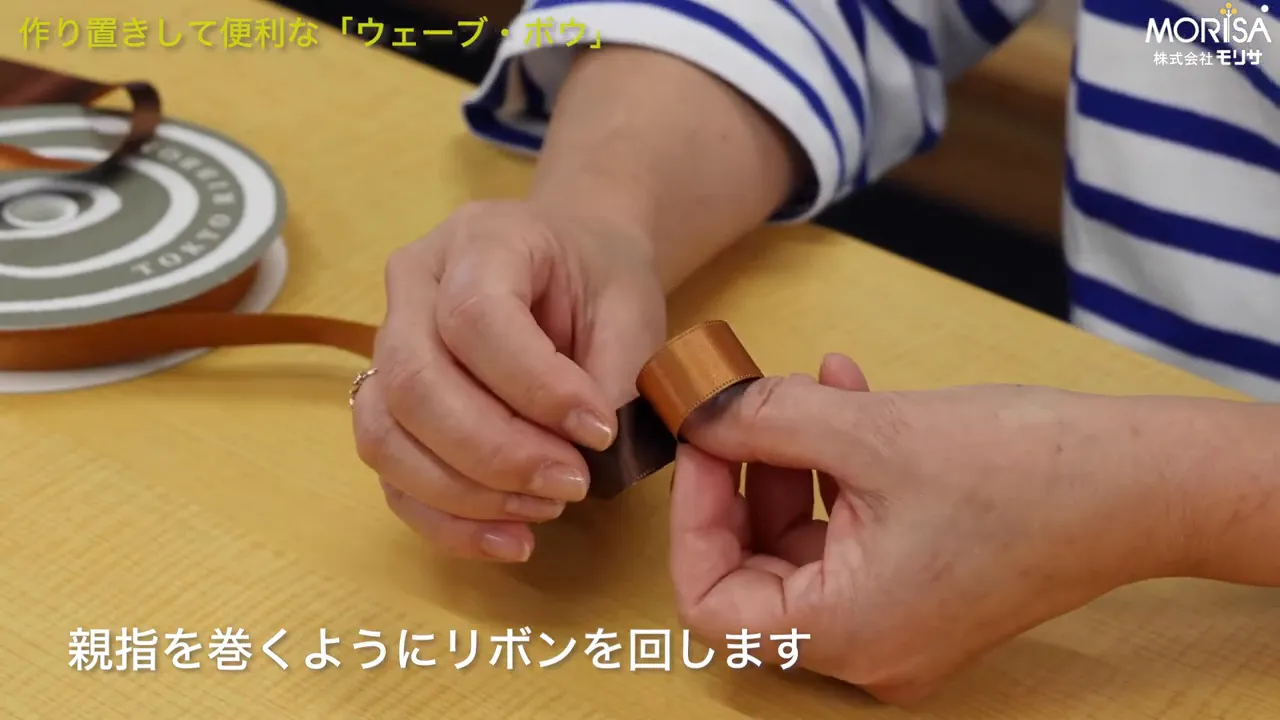 親指に巻いたリボンで輪を作る手元のクローズアップ