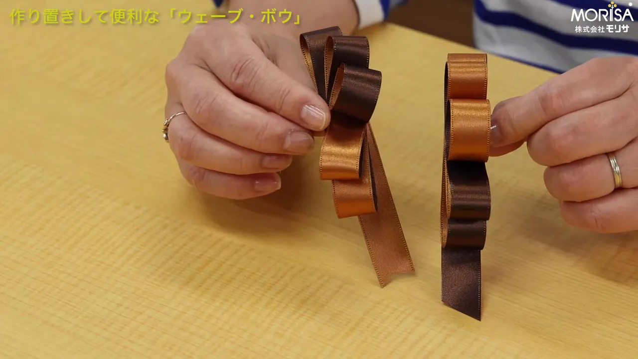 斜めにずらしたウェーブ・ボウの実例（茶色と金のリボン、手で微調整している様子）