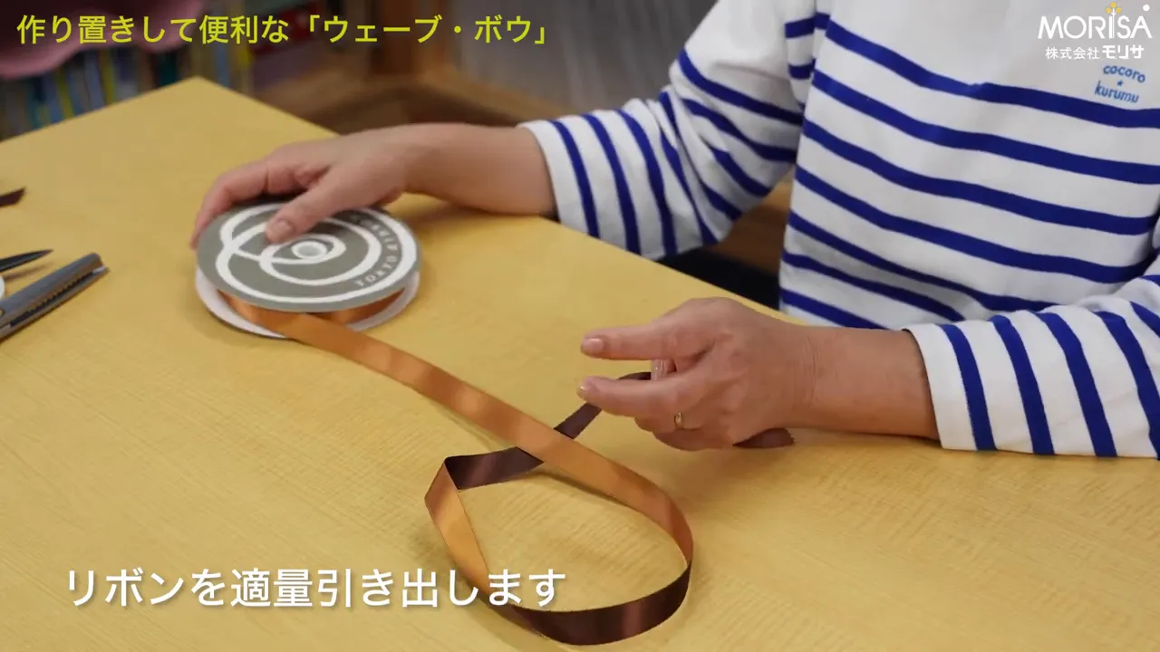 テーブルの上でスプールからリボンを引き出している手元
