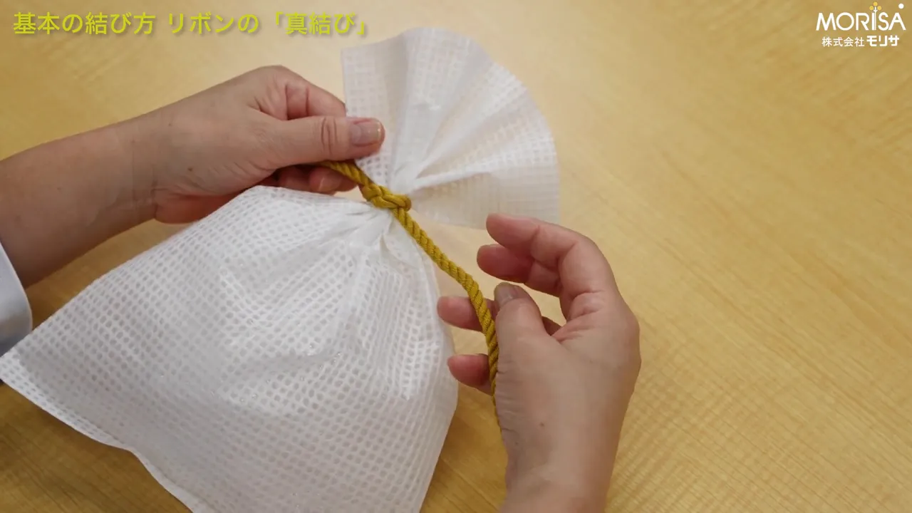 完成に近い真結びの基本形、袋の口を黄色い紐で結んだ手元の写真