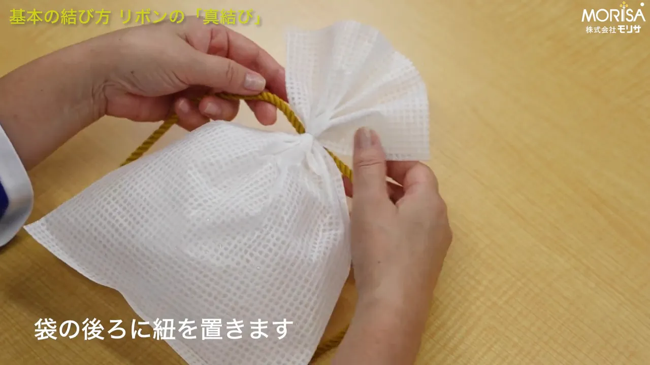 袋の後ろにひもの中心を置き、真結びの準備をする手元の写真