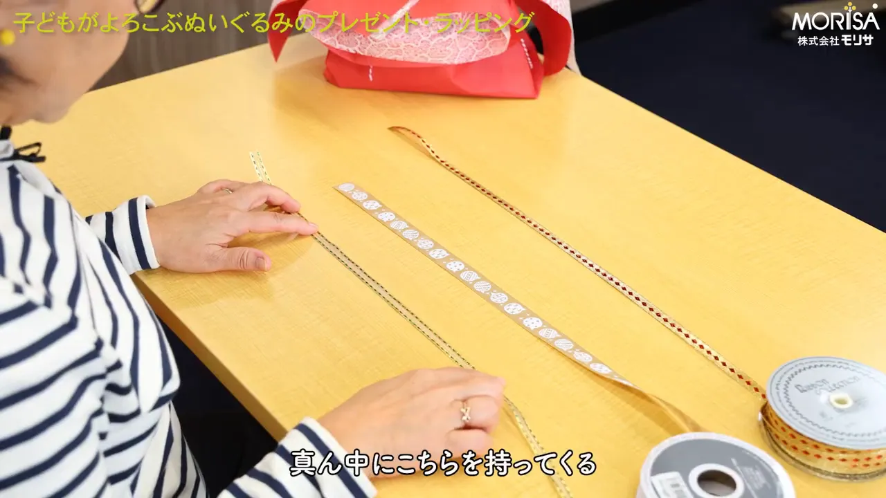 テーブルに3本のリボンが並べられ、ぬいぐるみが背景にある重ねリボン準備の写真。