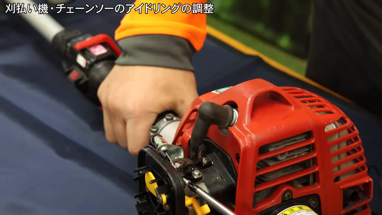 刈払い機のアイドリング調整ネジにドライバーを当てて回しているクローズアップ（ネジと工具がはっきり見える）